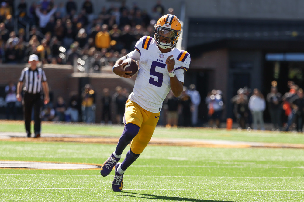 Jayden Daniels - wearing a white jersey with purple number 5 and yellow pants - runs in the open field