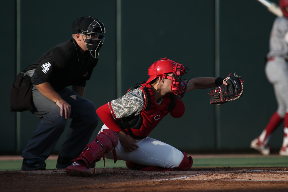 Jacob Cozart frames a pitch as the umpire watches.