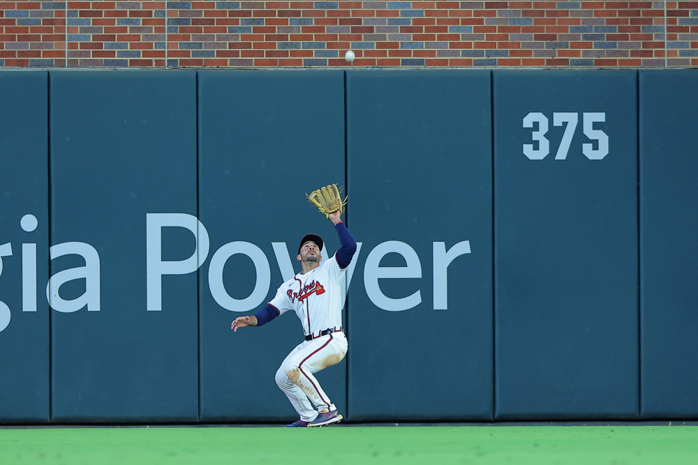 Ramon Laureano, in a white uniform, holds his glove up with his left hand and waits for a fly ball to come down.