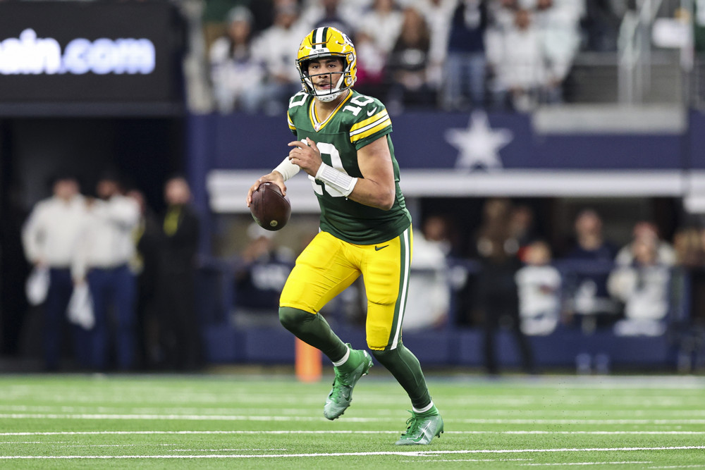 Jordan Love, in a Green Bay Packers uniform (green jersey, yellow pants and helmet) runs with the football.