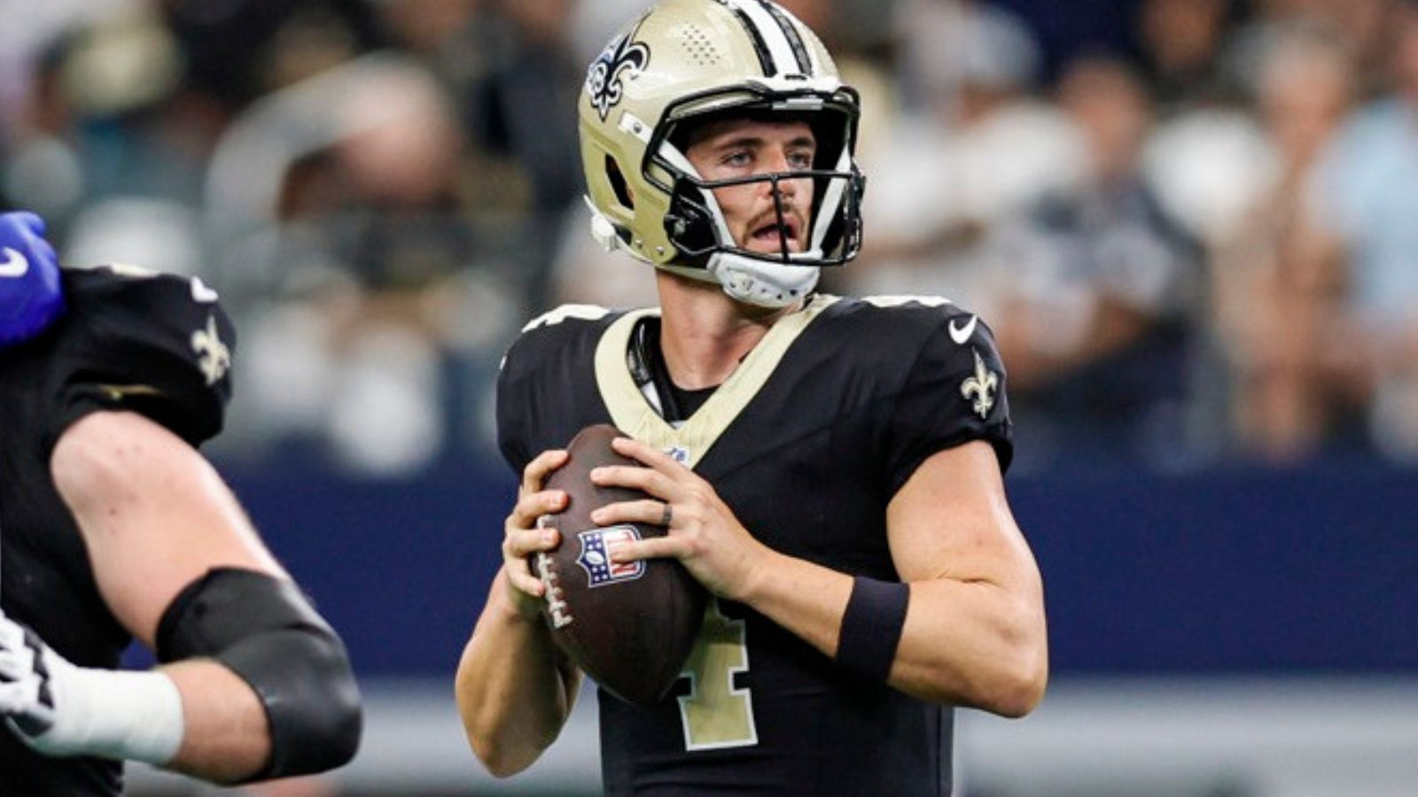 Derek Carr, in black jersey and gold helmet, prepares to throw a pass, holding the football with 2 hands in front of him