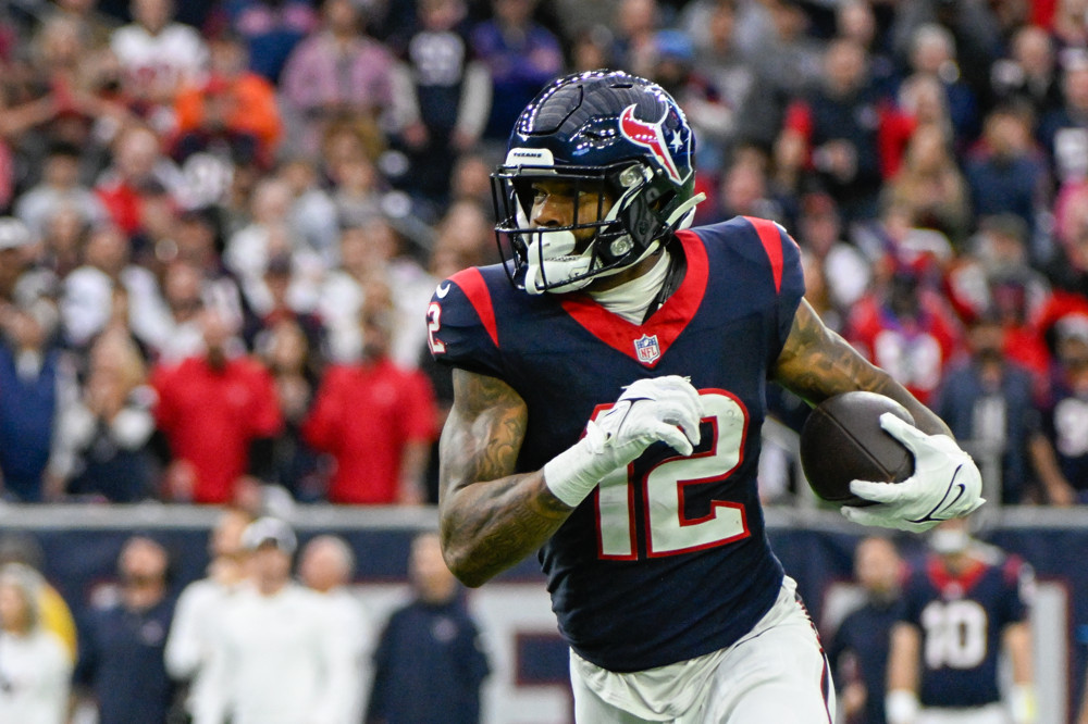 Nico Collins, wearing a blue jersey and white pants with a white 12 on the front, runs up the field after making a catch