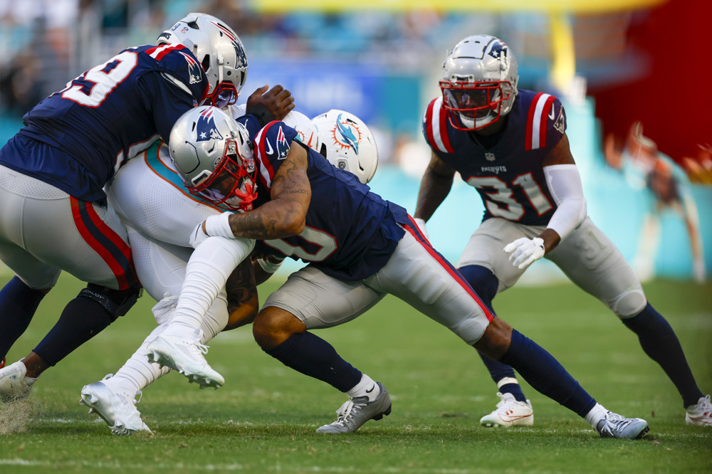 Christian Gonzalez (wearing a blue jersey with a 0 and grey pants) tackles Miami Dolphins running back De'Von Achane (wearing a white jersey with #28)