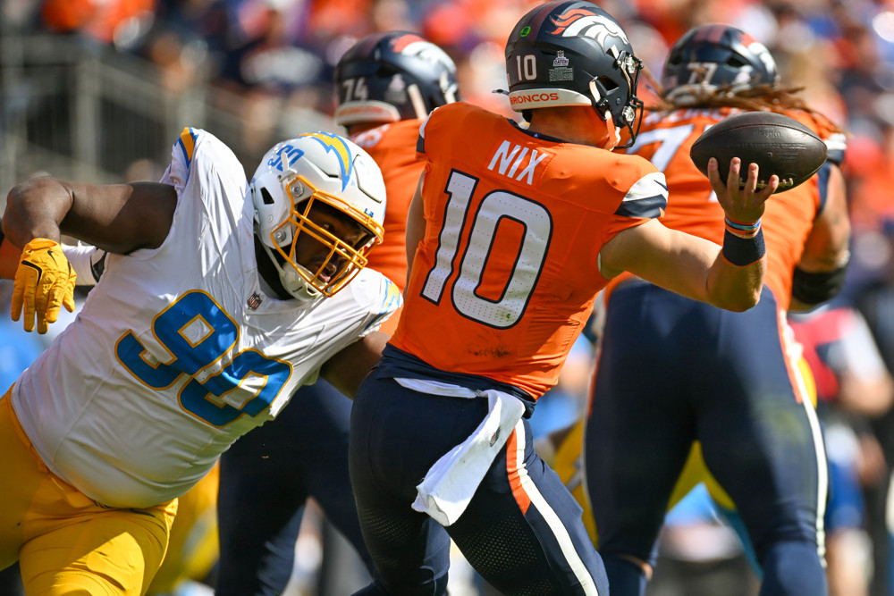 Bo Nix, in orange jersey and blue pants, attempts to make a throw as a player from the Chargers in a white jersey and white helmet comes lunging at him